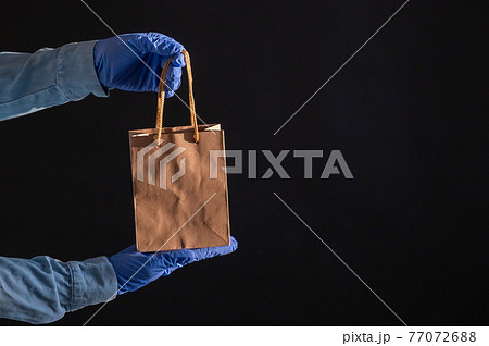 Express delivery to the epidemic of coronavirus. Closeup of courier's hands in rubber gloves with a paper bag with handles. Packaging made from eco friendly recycled material. Donation to quarantine. Express delivery to the epidemic of coronavirus. Closeup of courier's hands in rubber gloves with a paper bag with handles. Packaging made from eco friendly recycled material. Donation to quarantine. 77072688