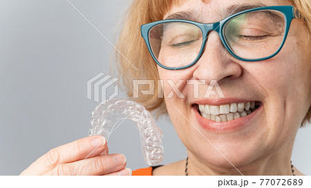 A happy elderly woman puts on transparent removable braces. Cosmetic dentistry for all ages 77072689