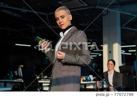 Pensive young woman with short hair uses mobile phone in office. 77072786