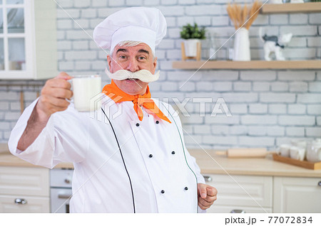 Elderly milkman drinks cow's milk in the kitchen. Elderly milkman drinks cow's milk in the kitchen. 77072834