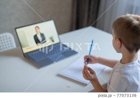 The boy communicates with a female teacher on a laptop webcam. Online lesson. Distance education in quarantine. A schoolboy is studying at home in the epidemic of coronavirus. 77073136