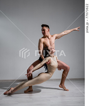 Acrobatic couple perform number on a white background. A duet of gymnasts rehearsing a performance with support. A man and a very flexible woman are dancing. Acrobatic couple perform number on a white background. A duet of gymnasts rehearsing a performance with support. A man and a very flexible woman are dancing. 77073622