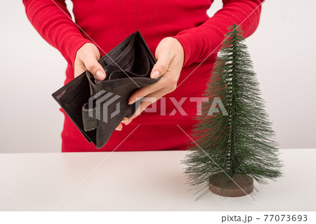 A woman is holding an empty purse next to a small artificial Christmas tree. The financial crisis during the holidays 77073693