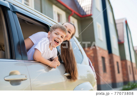 Traveling by car with the whole family. Happy Caucasian woman with son smiling sitting in the back seat of an SUV and looking out of a window. Car trip on summer vacation. Traveling by car with the whole family. Happy Caucasian woman with son smiling sitting in the back seat of an SUV and looking out of a window. Car trip on summer vacation. 77073808