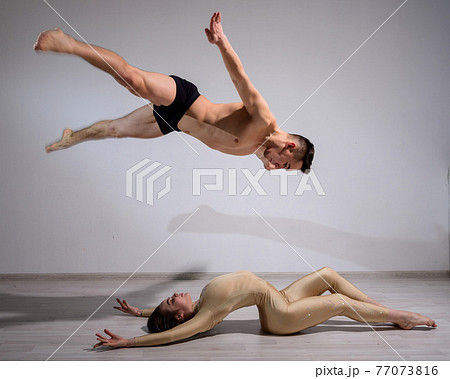 Acrobatic couple perform number on a white background. A duet of gymnasts rehearsing a performance with support. A man and a very flexible woman are dancing. 77073816