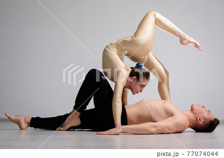 A duet of acrobats showing a pair trick. A woman in gymnastics overalls in a handstand over a shirtless man lies on his back. Very flexible circus performers. 77074044