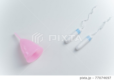 Pink menstrual cup and tampons on a white background. Comparison of personal hygiene products for women during menstruation Pink menstrual cup and tampons on a white background. Comparison of personal hygiene products for women during menstruation 77074697