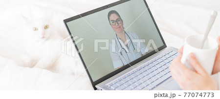 A faceless woman drinks an antipyretic and watches a video from a doctor recommendation. Online doctor consultation on a webcam without leaving your home. The cat lies in bed with a sick housewife. A faceless woman drinks an antipyretic and watches a video from a doctor recommendation. Online doctor consultation on a webcam without leaving your home. The cat lies in bed with a sick housewife. 77074773
