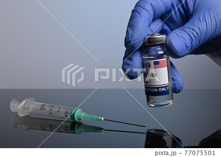 Gloved Hand Takes American Covid-19 Vaccine Jar 77075501