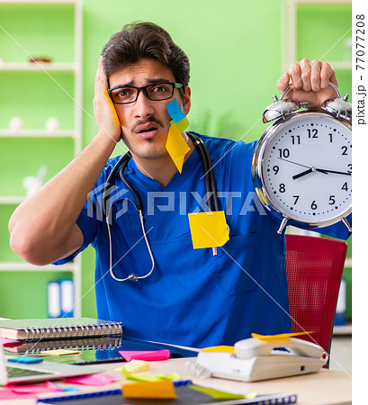 Young doctor sitting in hospital with many conflicting prioritie 77077208