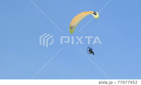 快晴の空を飛ぶ黄色いモーターパラグライダー 77077952