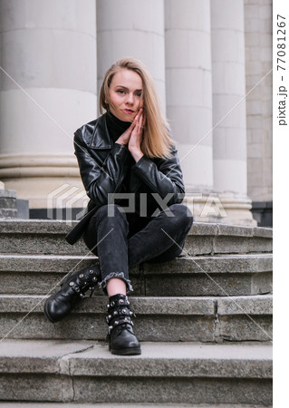 Portrait of young blonde woman with red lips wearing leather jacket on corporate building stairs. Career businesswoman. Urban street city lifestyle Portrait of young blonde woman with red lips wearing leather jacket on corporate building stairs. Career businesswoman. Urban street city lifestyle 77081267