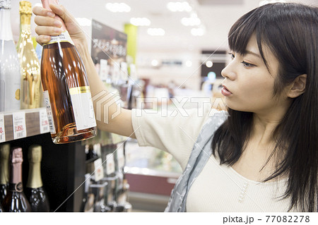 スーパーでワインを手に取る女性買い物客 77082278