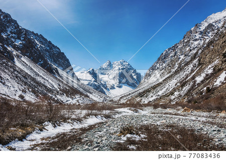 Idyllic winter landscape with hiking trail in the mountains. Rocks, snow and stones in mountain valley view. Mountain panorama. 77083436