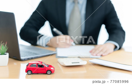 A car on desk envelope with man signing purchase documents in background. while hand complete the insurance policy, rental documents and loan document. concept guy buying new house A car on desk envelope with man signing purchase documents in background. while hand complete the insurance policy, rental documents and loan document. concept guy buying new house 77085996