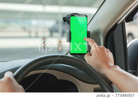 Mock up of man using mobile smart phone inside a car. Driver hand holding blank green screen smartphone, searching address and pin location via map navigator application, transportation 77086007