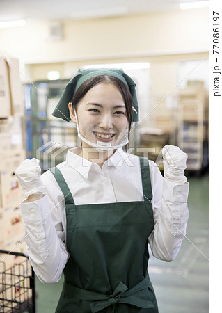 スーパーのバックヤードでマウスシールドをしたガッツポーズをする女性従業員 スーパーのバックヤードでマウスシールドをしたガッツポーズをする女性従業員 77086197