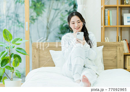 寝室でスマホを見る若い女性 77092965