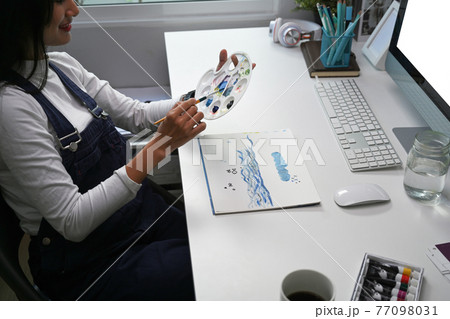 Cropped shot of young woman artist drawing painting in art studio with water colour on paper. Cropped shot of young woman artist drawing painting in art studio with water colour on paper. 77098031