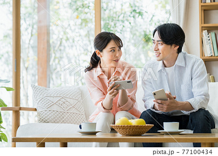 リビングでスマホを見る若い夫婦 リビングでスマホを見る若い夫婦 77100434