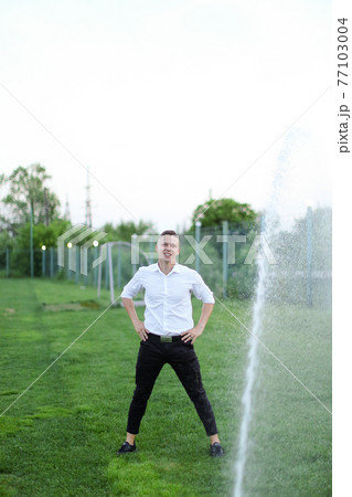 American boy standing on sprinkling football field near water jet. 77103004