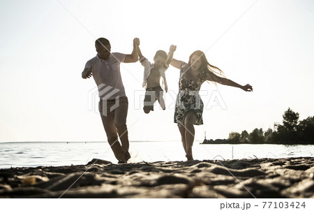Parents and son are running along the beach. Dark tones give the impression of vintage photography. Mom and Dad are holding the baby in their arms. The concept of a happy family and a wonderful life. 77103424