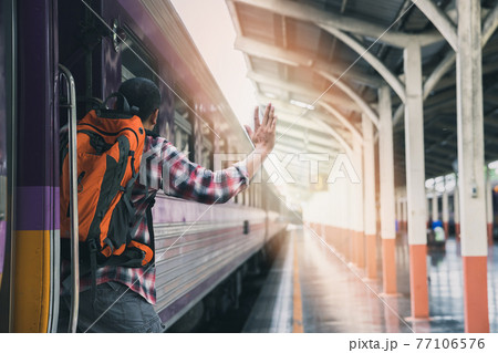 A man grabbed the handrail of the train door and waved his hand. People travel by local transport. A man grabbed the handrail of the train door and waved his hand. People travel by local transport. 77106576