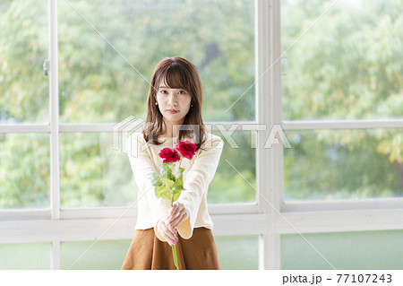 窓辺で薔薇を持ち告白する若い女性 77107243