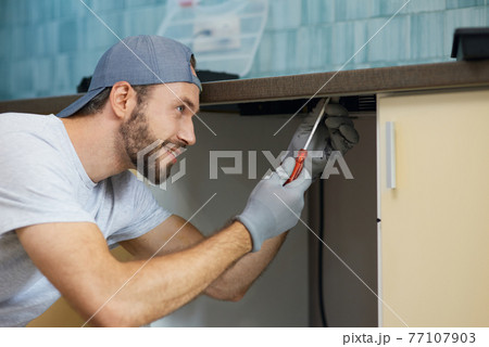 Doing it right. Portrait of young repairman, professional plumber looking concentrated while fixing sink pipe in the kitchen indoors 77107903
