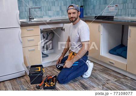 Young caucasian male worker on floor next to kitchen sink Young caucasian male worker on floor next to kitchen sink 77108077
