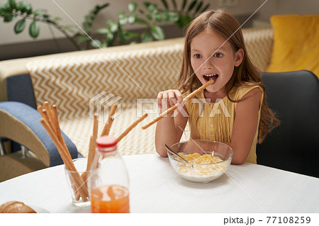 Cute little caucasian girl having breakfast at home and smiling, eating cereals with milk and snacks Cute little caucasian girl having breakfast at home and smiling, eating cereals with milk and snacks 77108259