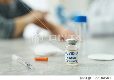 Coronavirus vaccine and medical syringe on table in clinic 77108501