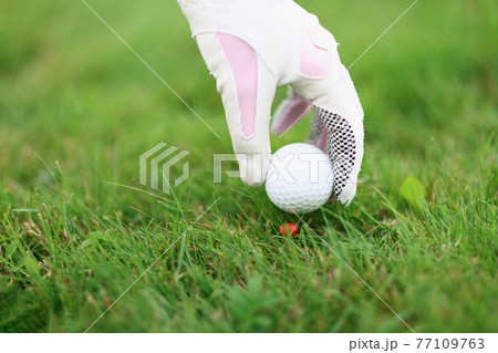 Hand in golf glove puts ball on golf tee Hand in golf glove puts ball on golf tee 77109763