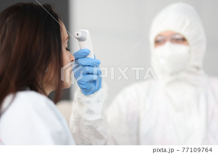 Doctor in protective suit measures woman temperature with thermometer 77109764