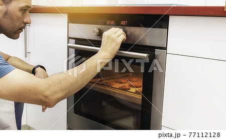 Young man connecting the oven to make cookies Young man connecting the oven to make cookies 77112128