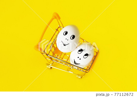 two white eggs with cheerful faces in shopping cart on yellow background two white eggs with cheerful faces in shopping cart on yellow background 77112672