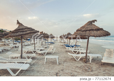 empty Tunisian beach with old sun loungers and sun canopies 77112674