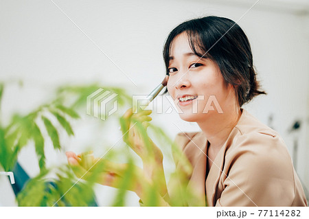 笑顔でメイクをする若い女性 77114282