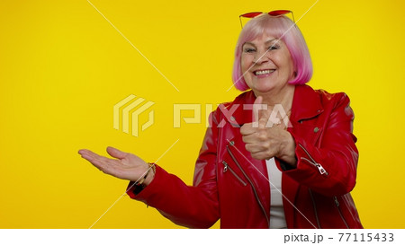 Senior old granny woman showing thumbs up and pointing at left on blank space, advertisement logo 77115433