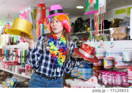 Young woman choosing funny headdresses 77120653