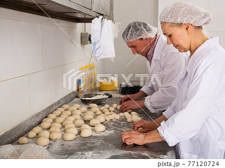 Two bakers portioning and shaping dough 77120724