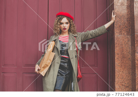 Fashion model woman in red french beret standing near red wooden door 77124643