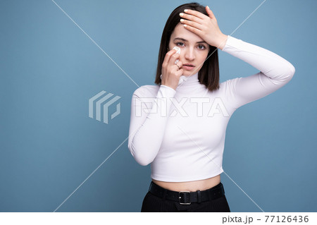 A woman with symptoms of a cold and headache holds in her hand in the studio on a blue background A woman with symptoms of a cold and headache holds in her hand in the studio on a blue background 77126436