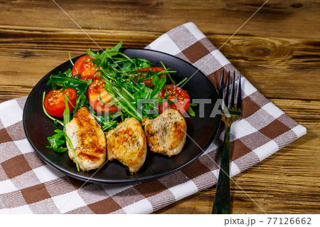 Fried chicken breast with salad of fresh arugula and cherry tomatoes on wooden table 77126662