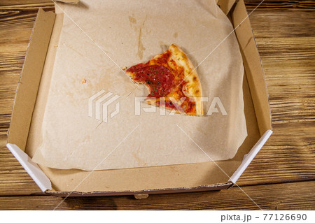 Bitten slice of pizza in cardboard box on a wooden table. Concept for home delivery of food, fast food, delivery of pizza Bitten slice of pizza in cardboard box on a wooden table. Concept for home delivery of food, fast food, delivery of pizza 77126690