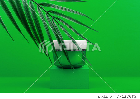 Green glossy cosmetic jar with white cap on green podium against green background with palm leaf Green glossy cosmetic jar with white cap on green podium against green background with palm leaf 77127685