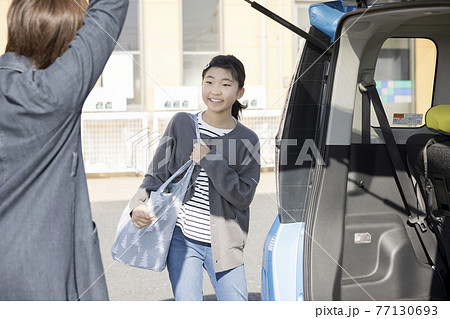 スーパーで買い物をしたマイバッグを運ぶ小学生女の子とバックドアを開けるお母さん お手伝いイメージの写真素材