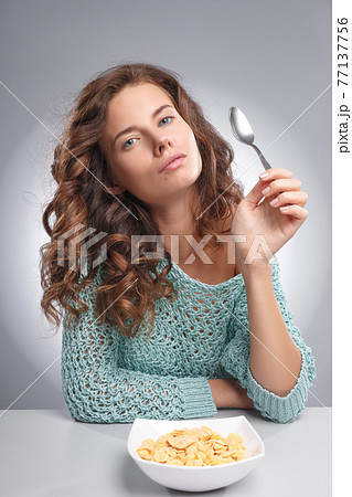 A pretty young girl has corn flakes with milk on a gray background A pretty young girl has corn flakes with milk on a gray background 77137756