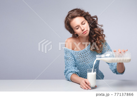 Beautiful woman pour out milk into glass Beautiful woman pour out milk into glass 77137866