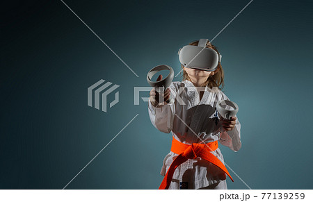Caucasian little girl in karate uniform playing video games with VR headset 77139259